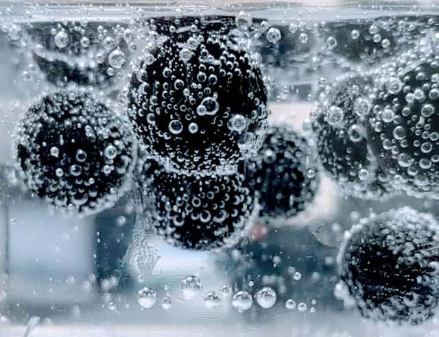 Spheres covered in bubbles are lifted upward in carbonated water.
