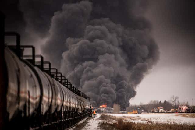 Smoke billows at the back of a black freight train.