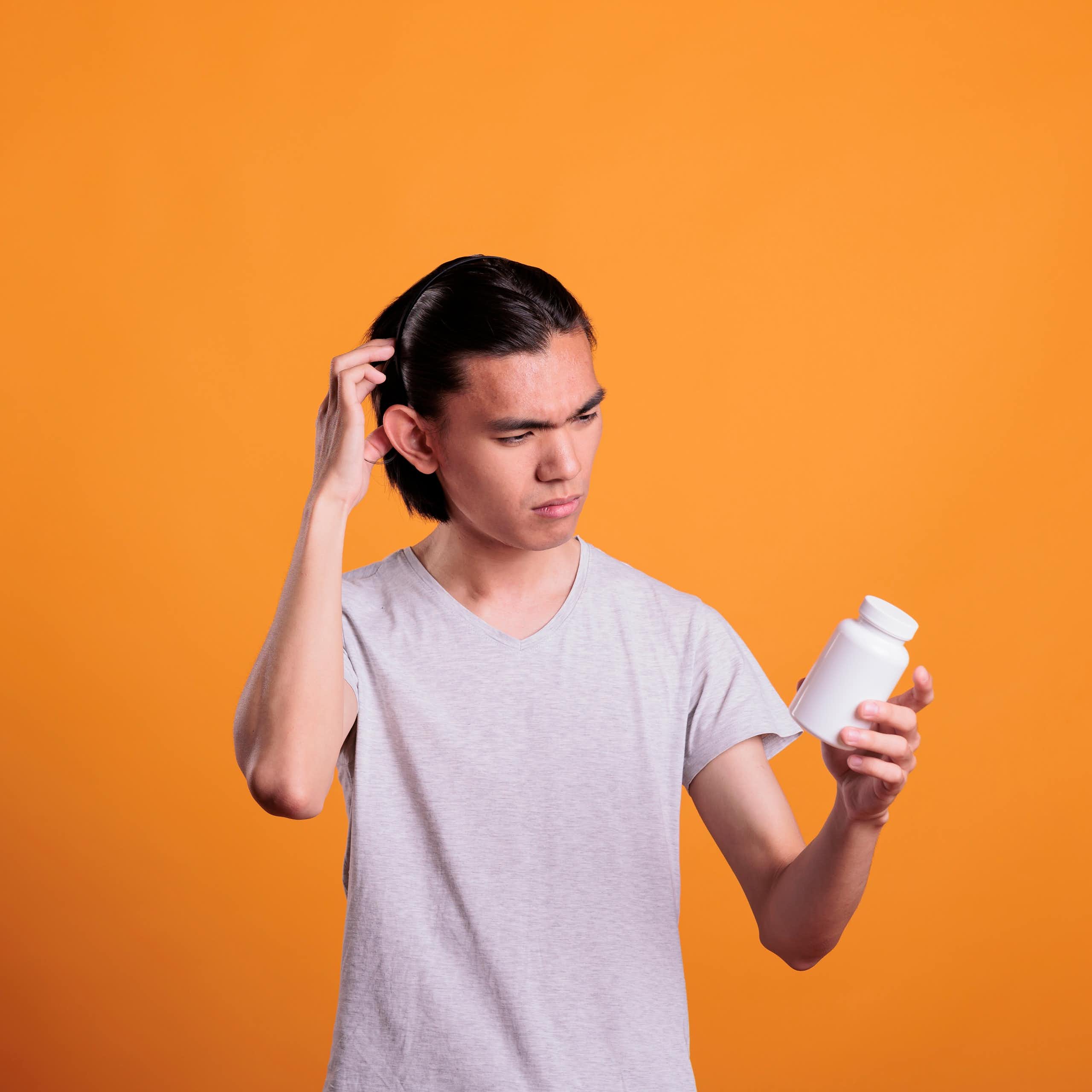 A man in a white T-shirt looking at a medication bottle against an orange background