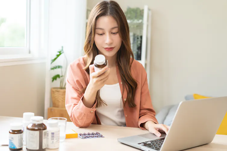 A woman reading a drug label in front of a laptop computer