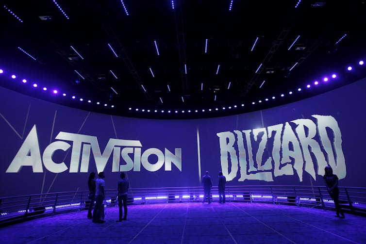 People walk in front of a wall with the Activision and Blizzard logos on it