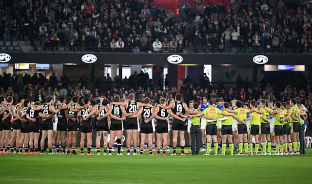 Players and umpires link arms for a moment of silence for victims of gender-based violence ahead of a Round 8 AFL game