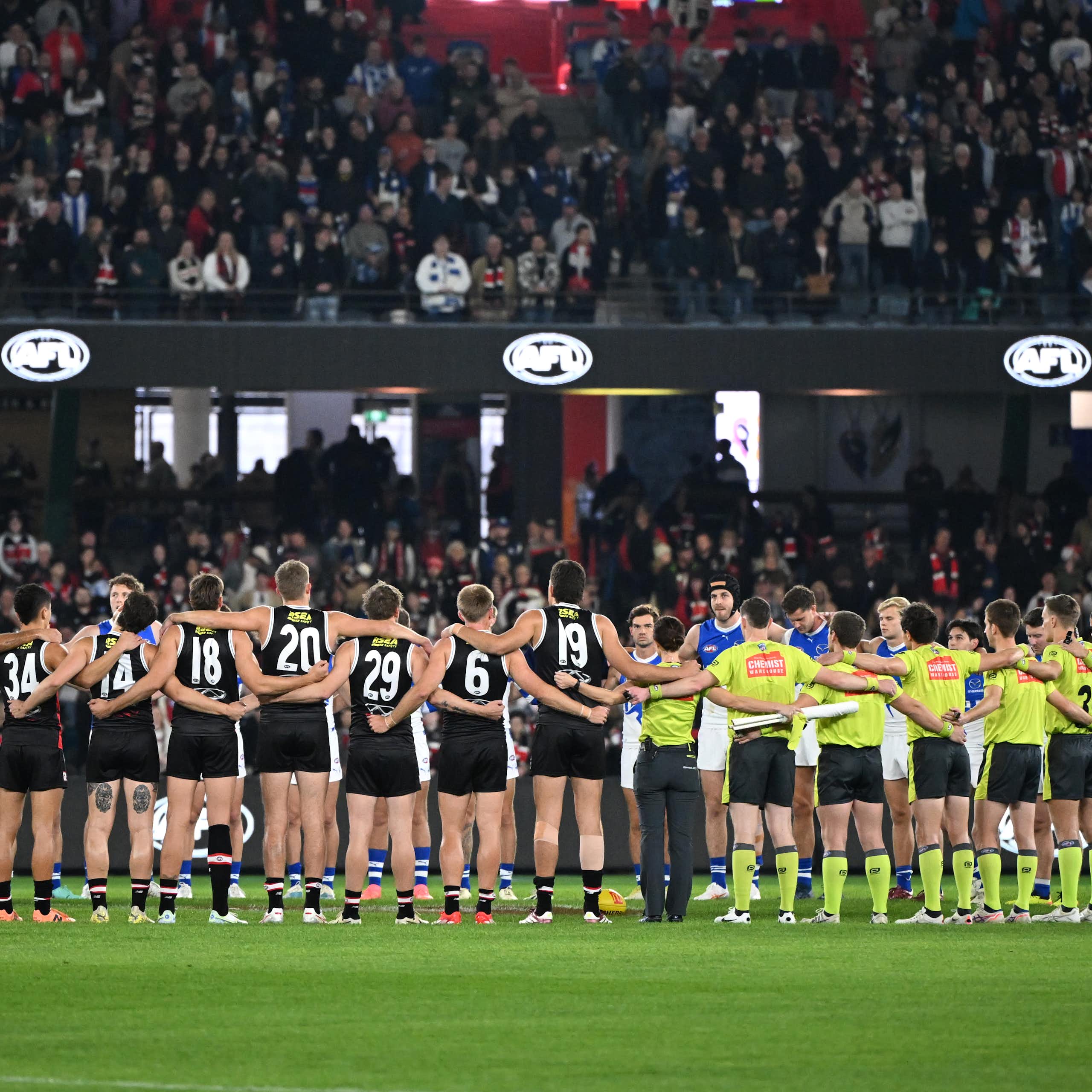 Players and umpires link arms for a moment of silence for victims of gender-based violence ahead of a Round 8 AFL game