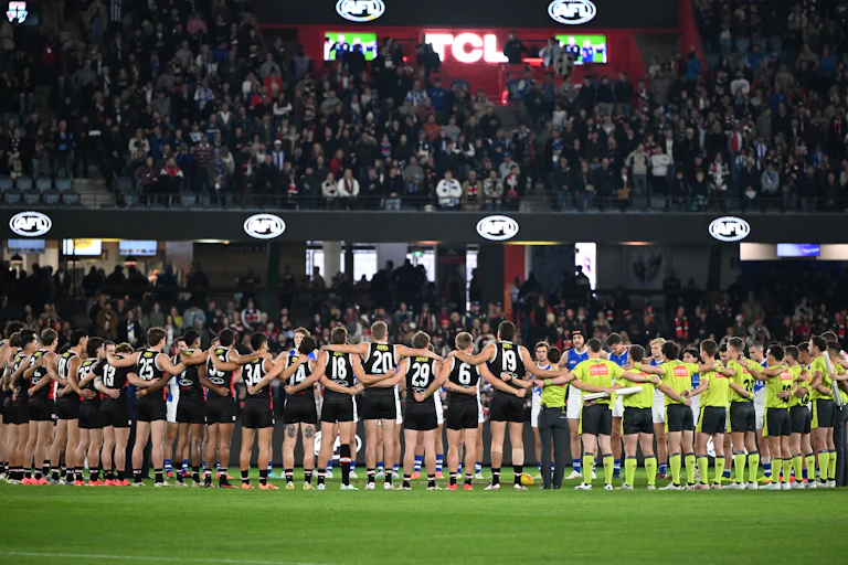 Players and umpires link arms for a moment of silence for victims of gender-based violence ahead of a Round 8 AFL game