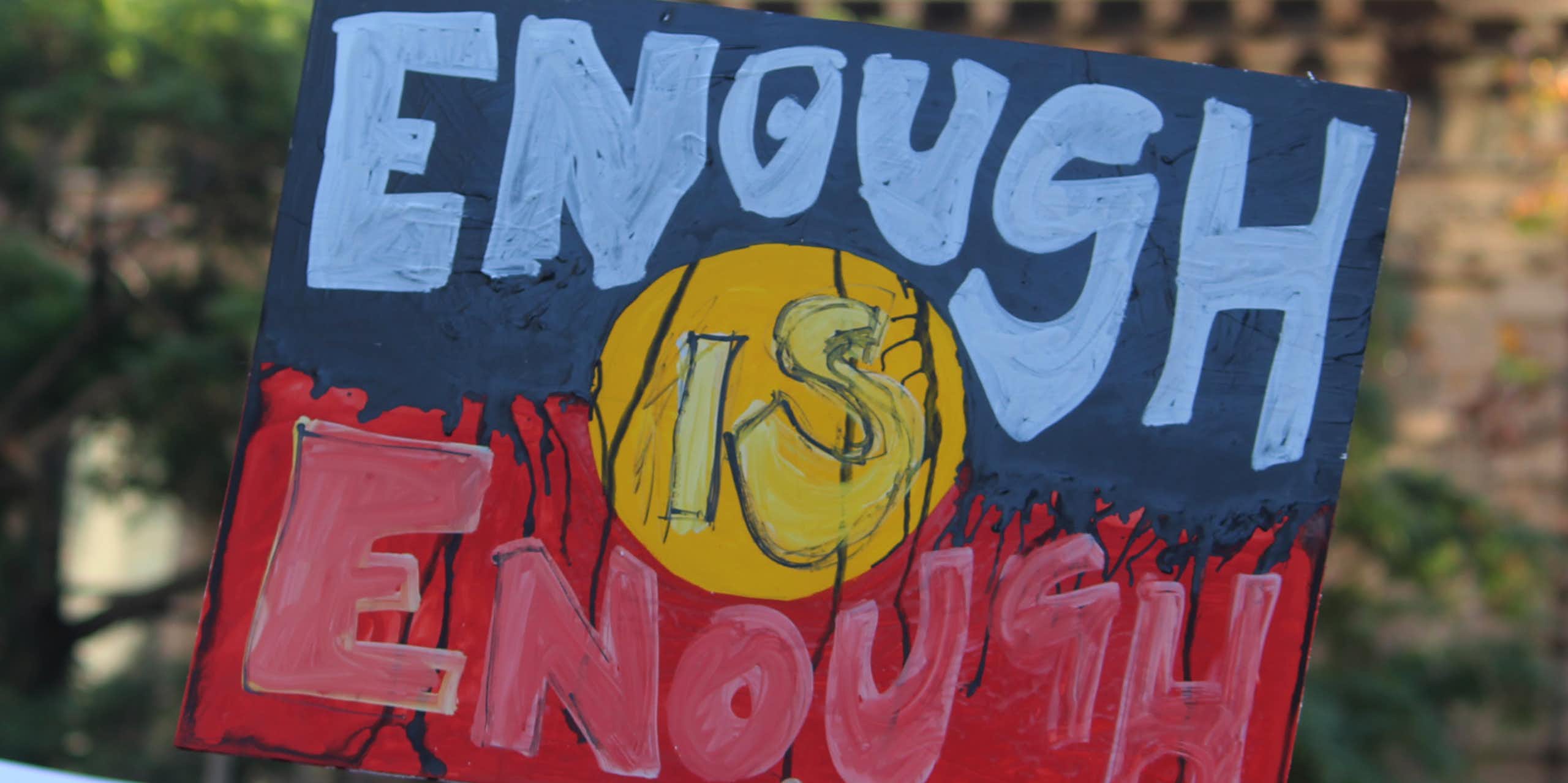 A sign in the colours and style of the Aboriginal flag saying enough is enough.