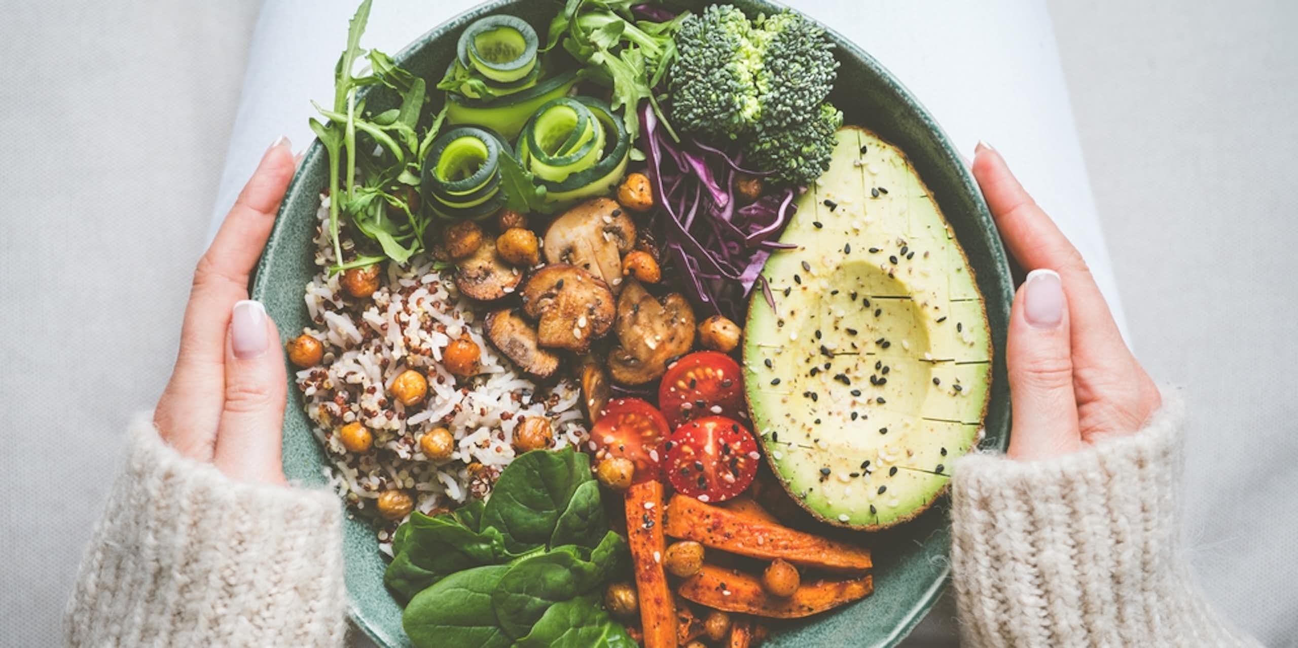 Woman holding bowl of vegan food (avocado, veggies, rice) on lap