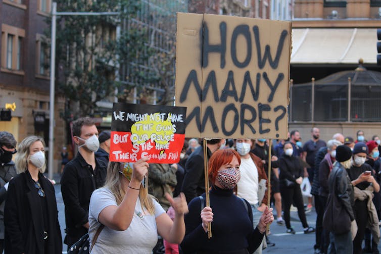 A protest with one woman holding a sign that reads how many more?