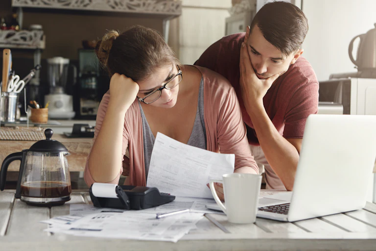A young man and woman sit at a kitchen counter looking over papers
