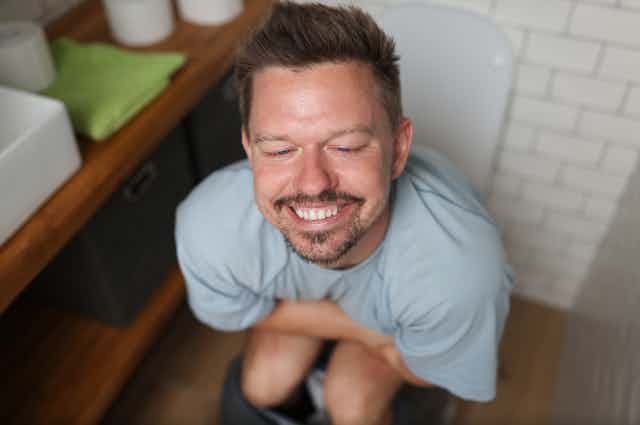 Smiling man sitting on toilet