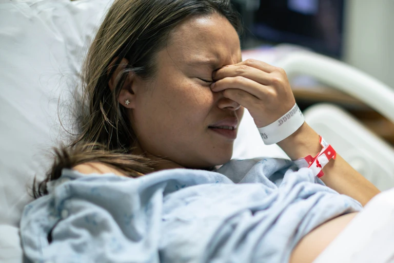 Distressed woman in hospital bed, hand clutching bridge of nose