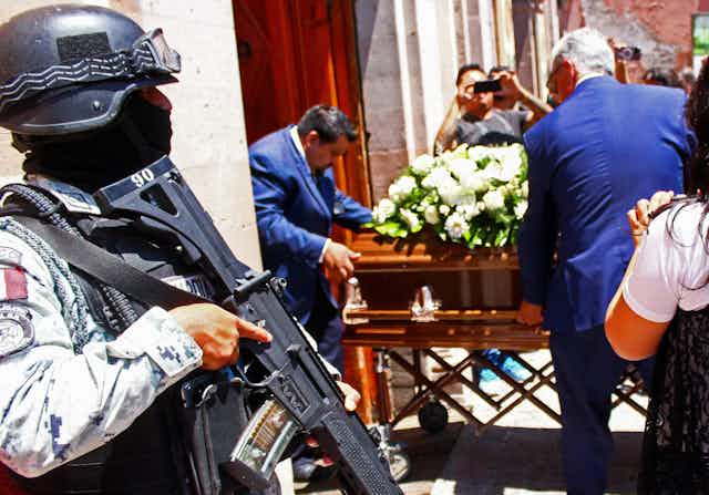 An armed guard standing outside a cathedral as a coffin is carried through the door.