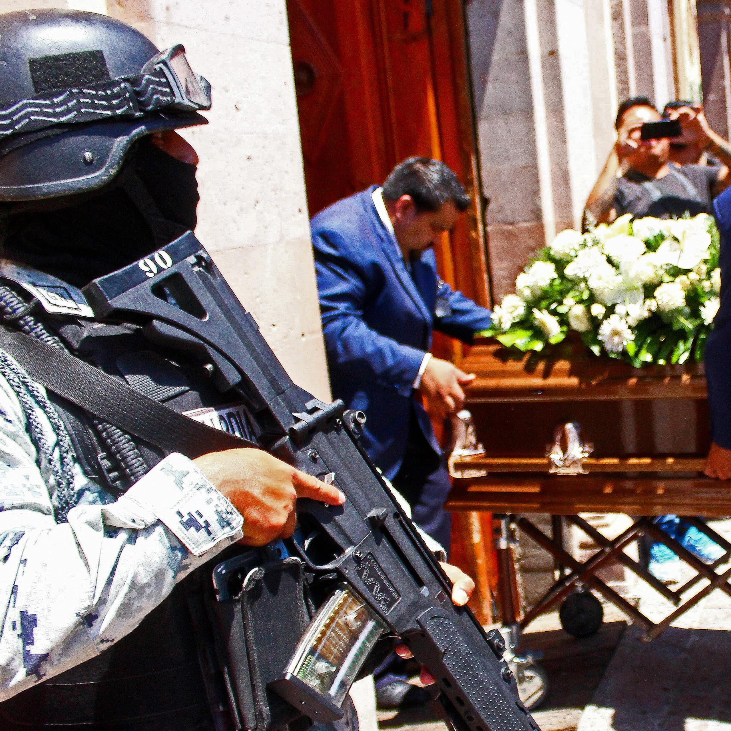 An armed guard standing outside a cathedral as a coffin is carried through the door.