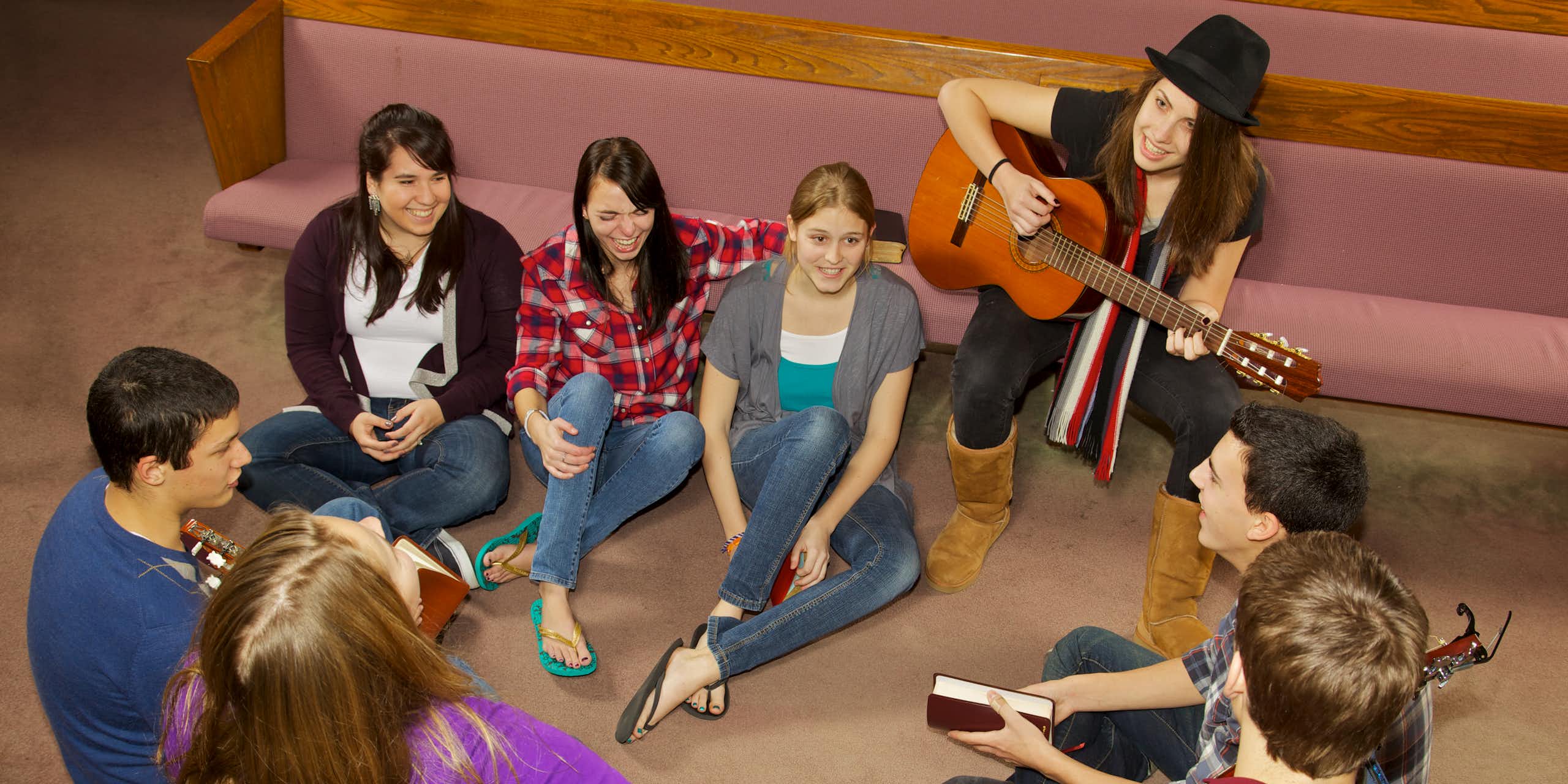 A group of young people sitting on the floor near church pews.