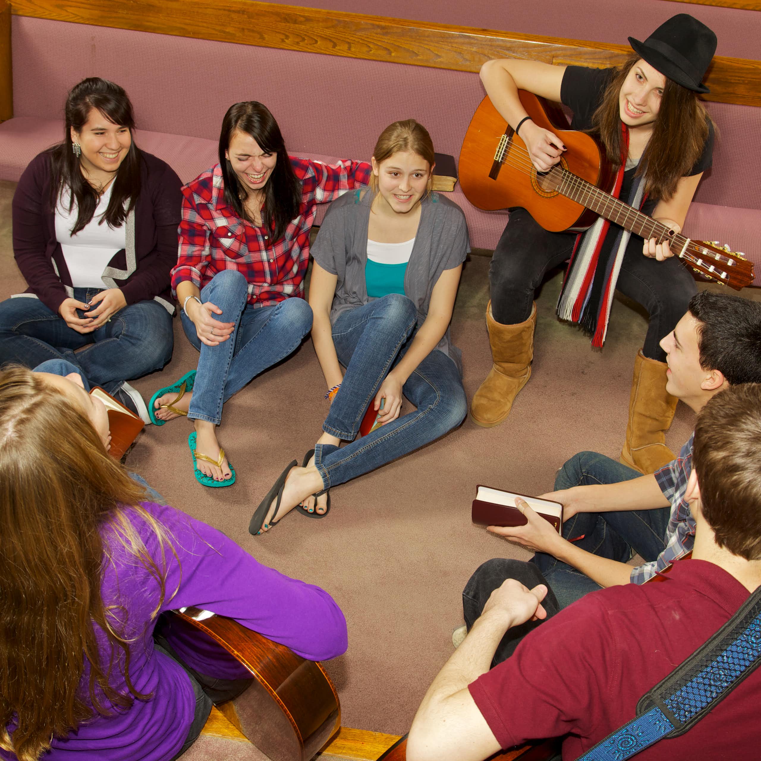 A group of young people sitting on the floor near church pews.