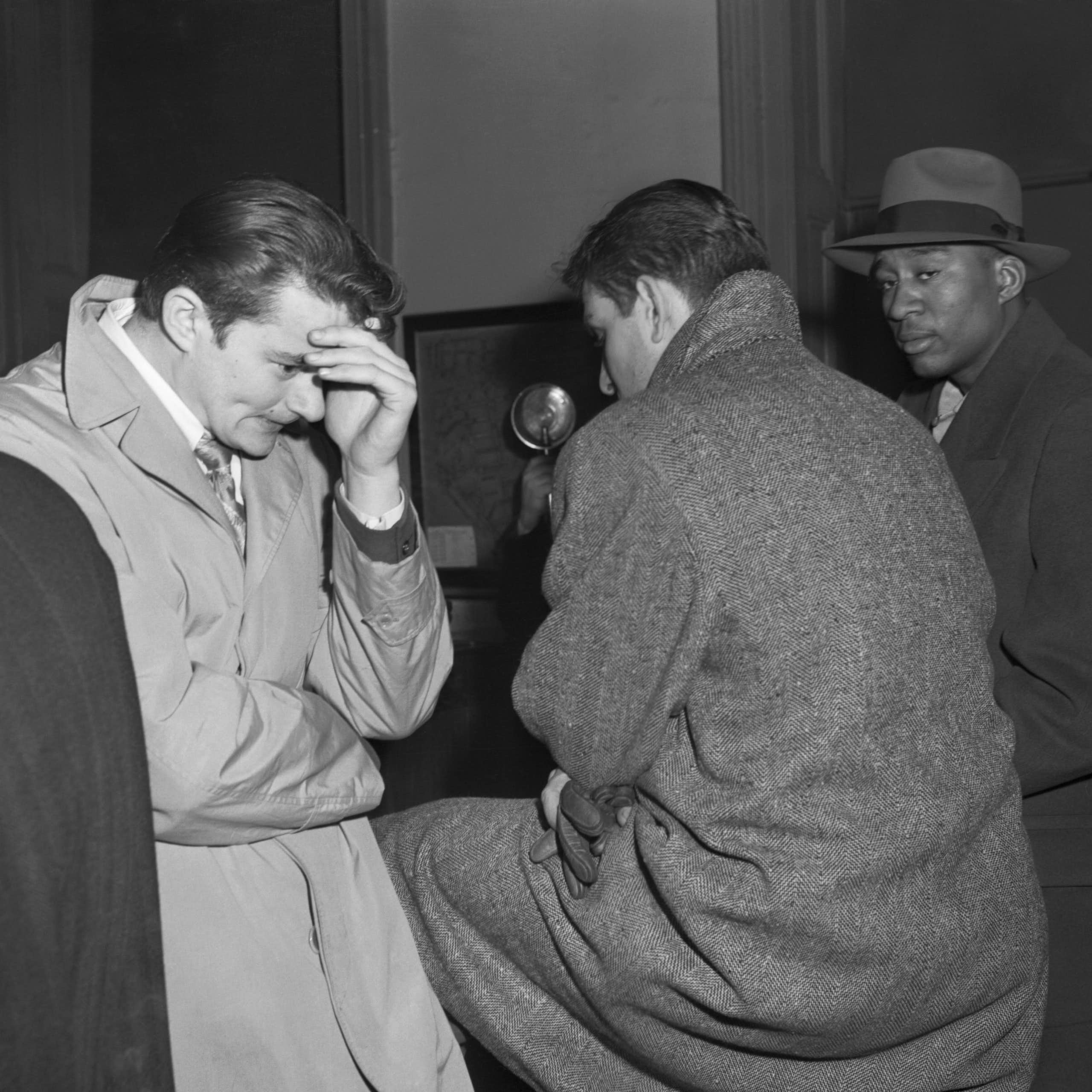Three young men -- one hiding his face behind his hand in apparent shame, another looking warily at the photographer -- are seen waiting in a police station.