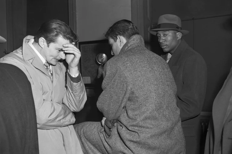 Three young men -- one hiding his face behind his hand in apparent shame, another looking warily at the photographer -- are seen waiting in a police station.