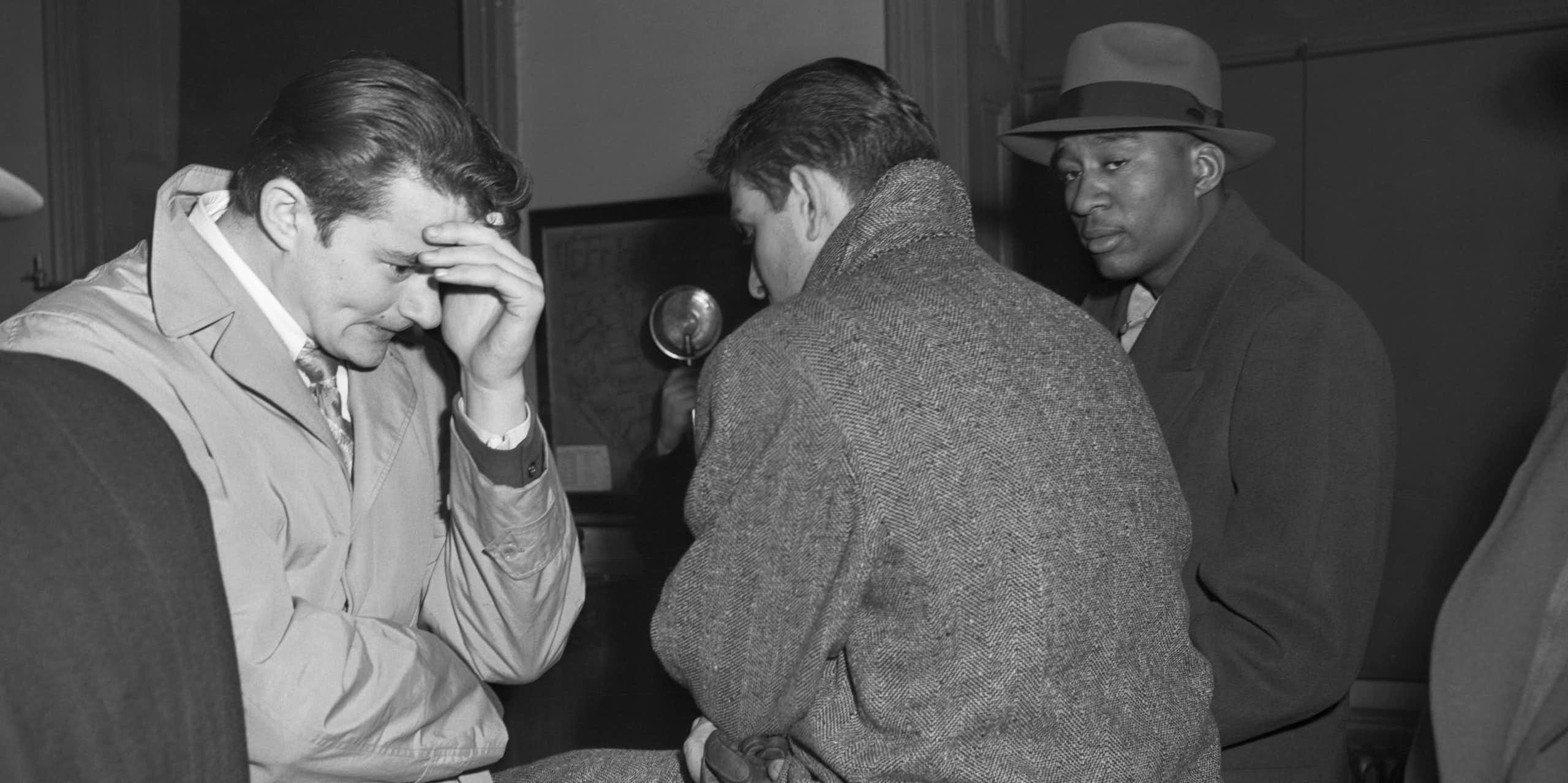 Three young men -- one hiding his face behind his hand in apparent shame, another looking warily at the photographer -- are seen waiting in a police station.