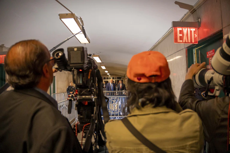 People with a video camera filming someone speaking across a hall.