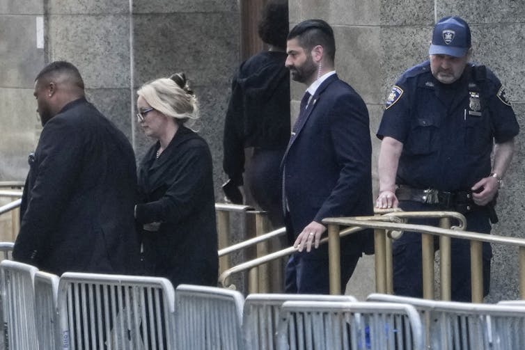A woman with blond hair walking out of a large building next to metal barricades.