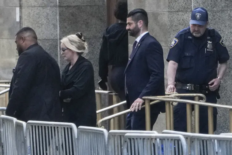 A woman with blond hair walking out of a large building next to metal barricades.