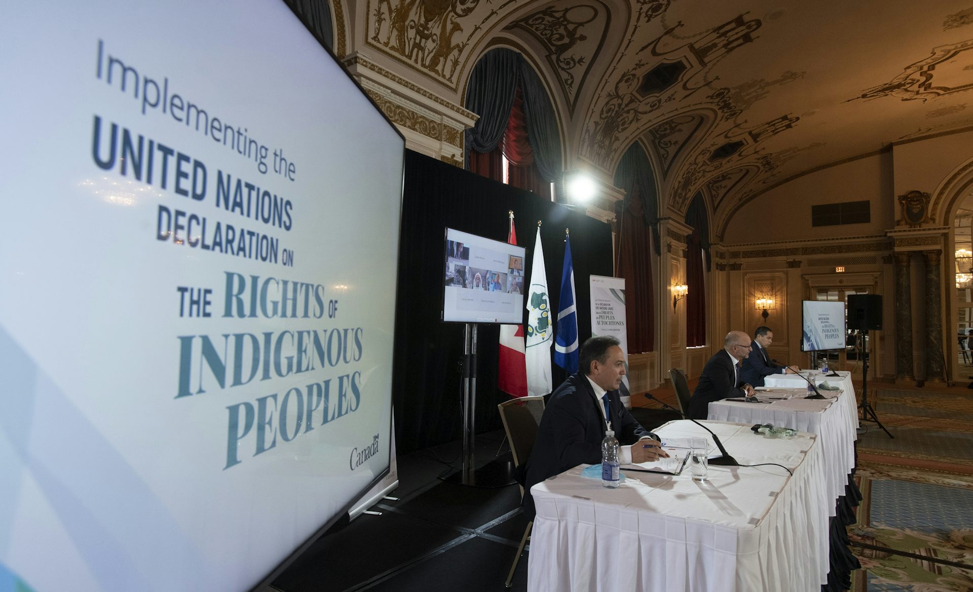 A man sits at a table with other men with a sign to his right that reads United Nations Declaration on the Rights of Indigenous Peoples.