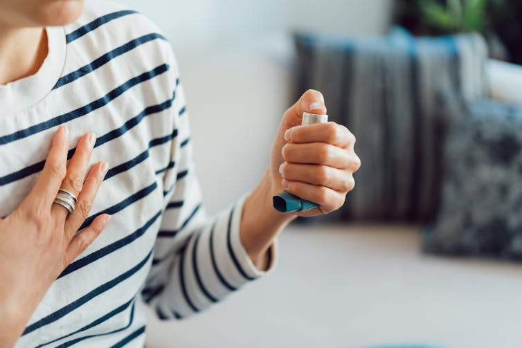 Person with one hand to chest and other hand clutching an inhaler