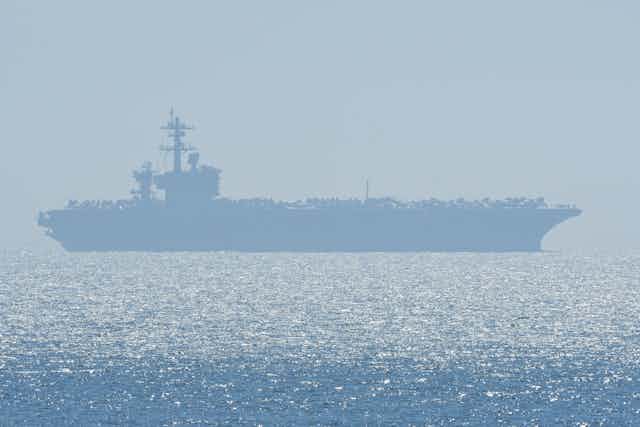 Aircraft carrier silhouetted in shimmering sea