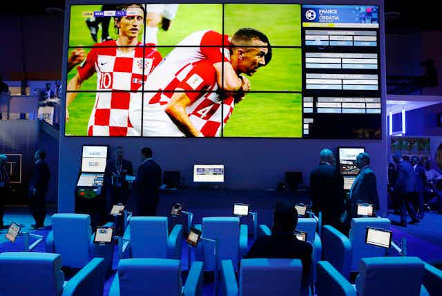 A soccer game displayed one a large screen above a row of sports betting kiosks
