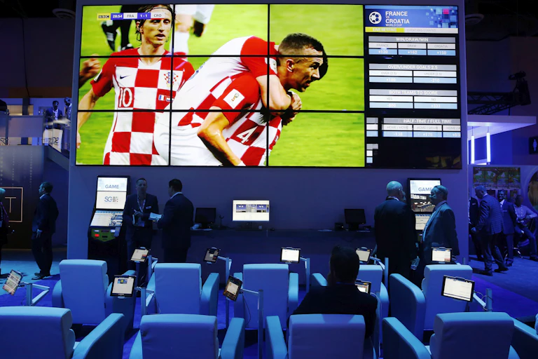 A soccer game displayed one a large screen above a row of sports betting kiosks