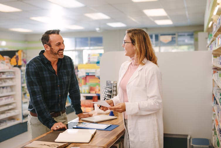A male customer is talking to a female pharmacist. Both are smiling.