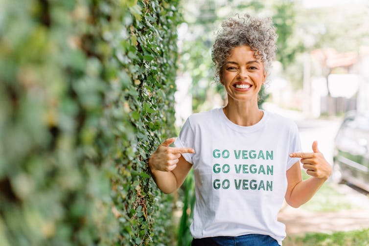 Woman wearing and pointing to her t-shirt with 'Go vegan' logo