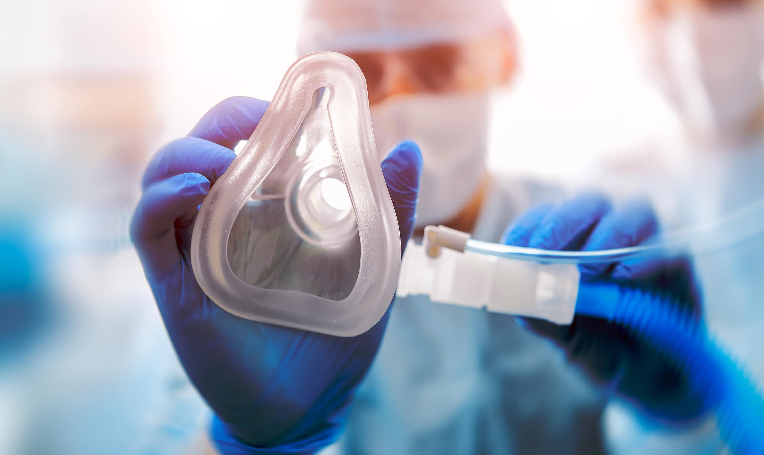 A hand in a blue nitrile glove placing an oxygen mask towards the camera.