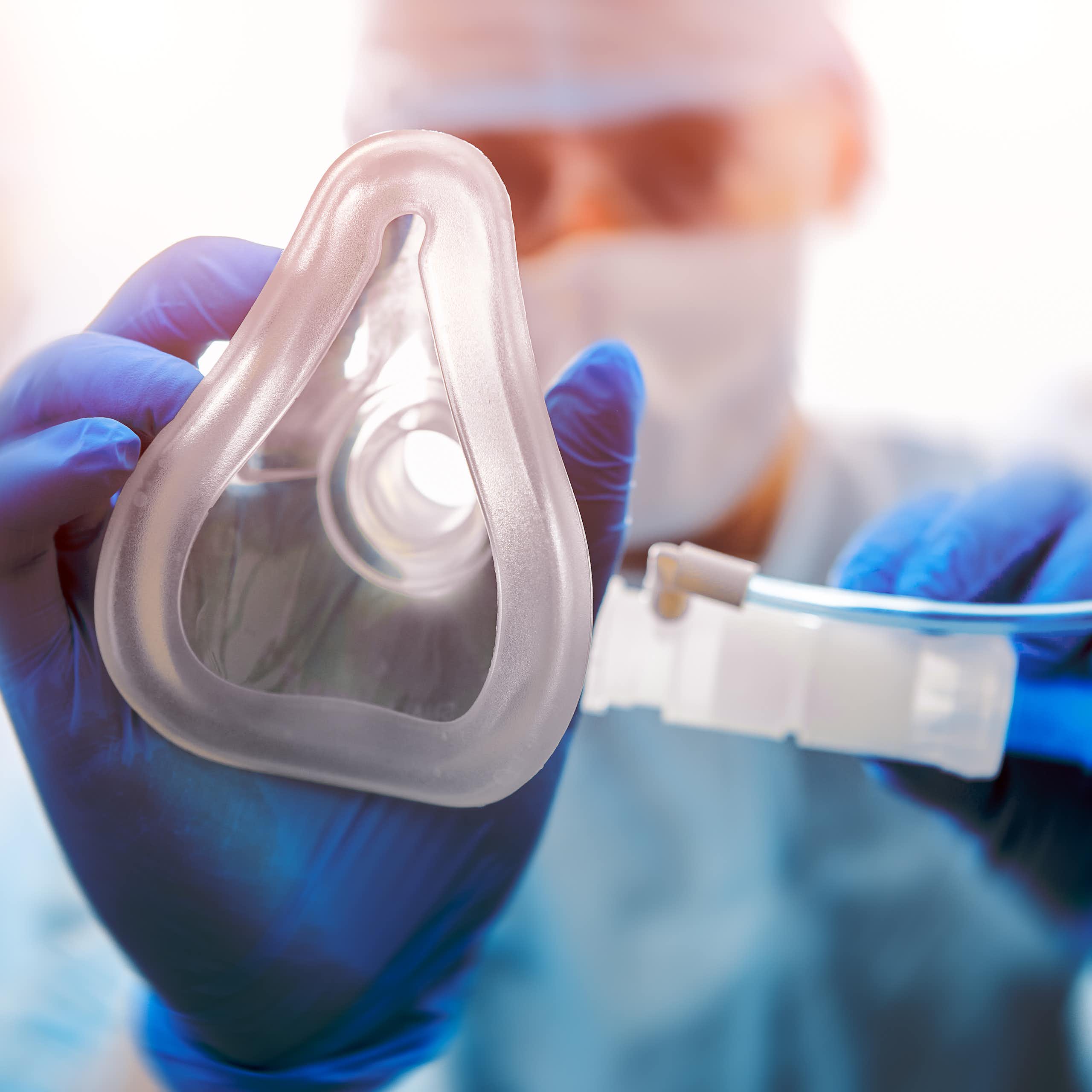 A hand in a blue nitrile glove placing an oxygen mask towards the camera.