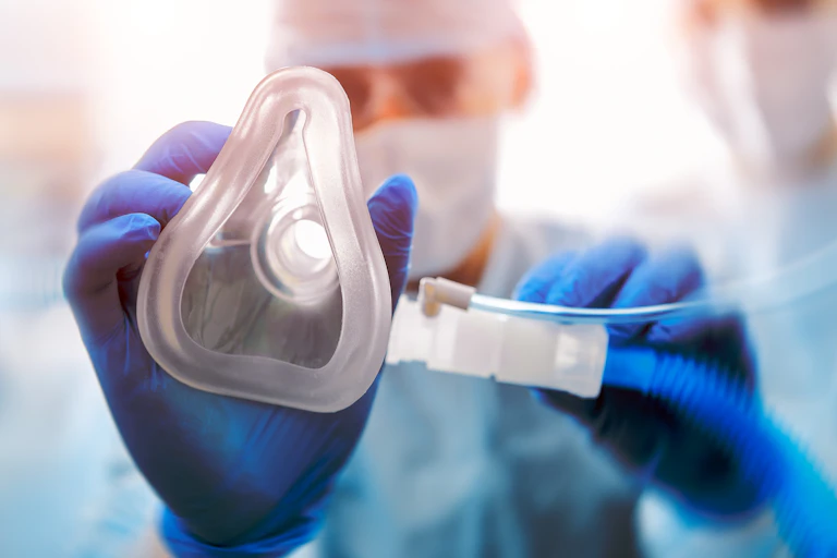A hand in a blue nitrile glove placing an oxygen mask towards the camera.