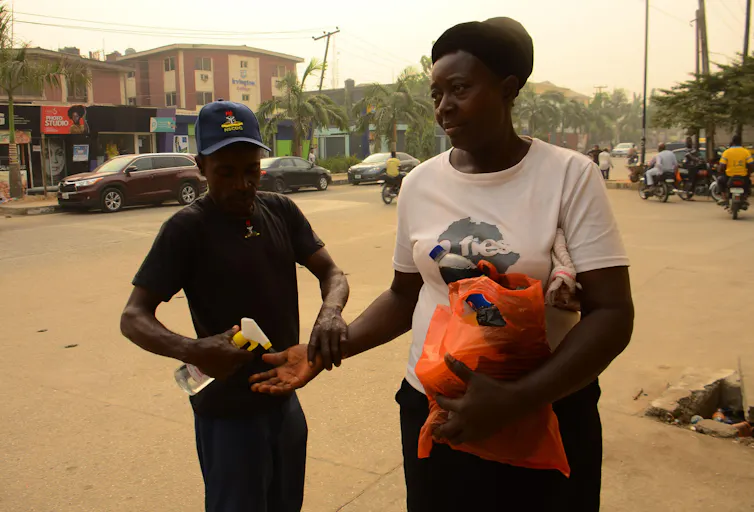 A Nigerian Security and Civil Defence Corps official sprays a woman's hand with hand sanitiser during a Lassa fever outbreak.
