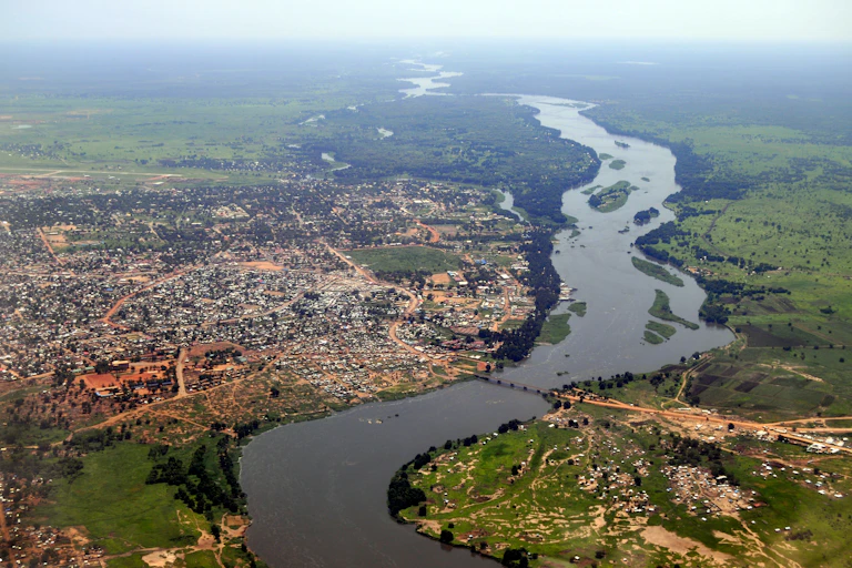 An aerial photograph of a river wending its way through green valleys, flanked on the left of the image by a sprawling city