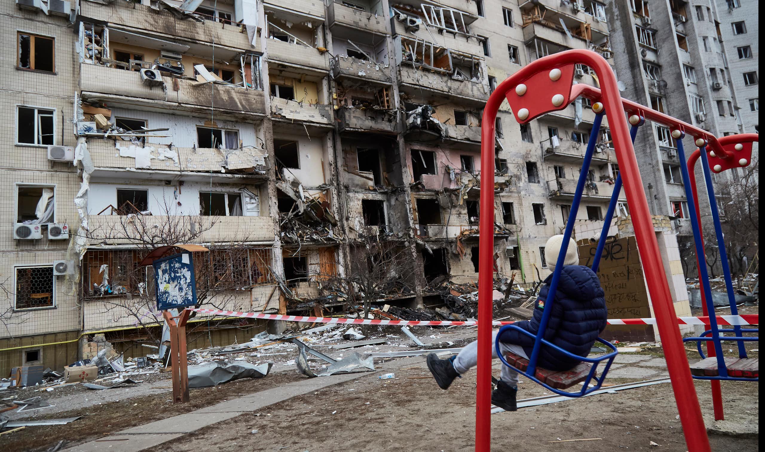 A child on a swing looks at a destroyed building.