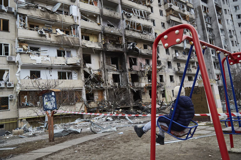 A child on a swing looks at a destroyed building.