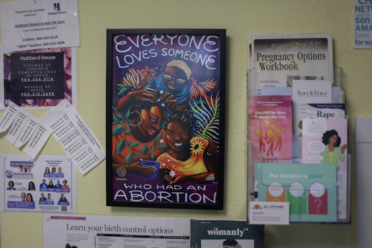 A colorful poster reads, “Everyone loves someone who has an abortion,” and is surrounded by other papers on the wall.