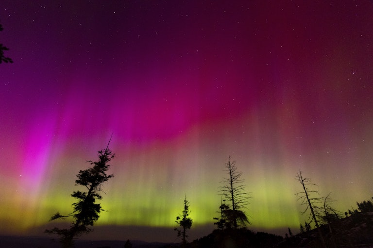 The night sky with magenta and red shades up high and bright green lower at the horizon.