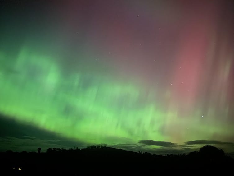 A mottled night sky with bright green lights and pink streaks above them.