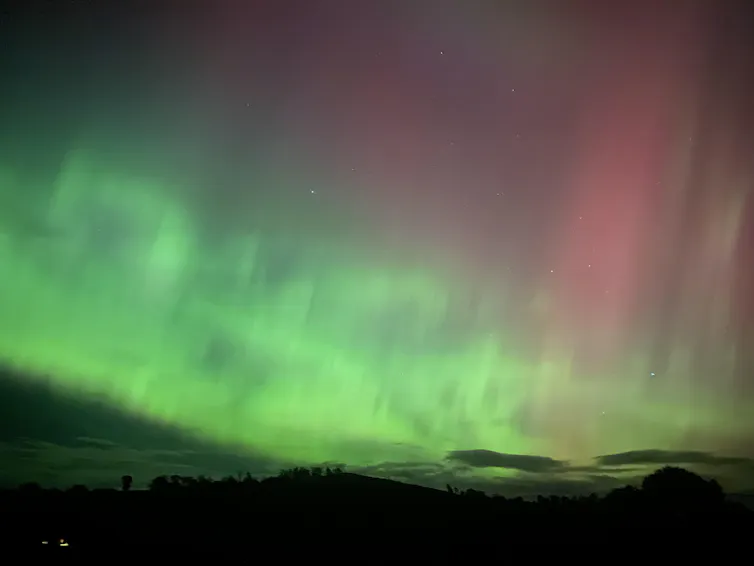 A mottled night sky with bright green lights and pink streaks above them.