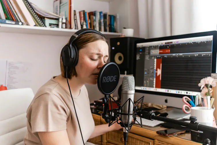 A person sitting at a home studio recording vocals on a microphone.