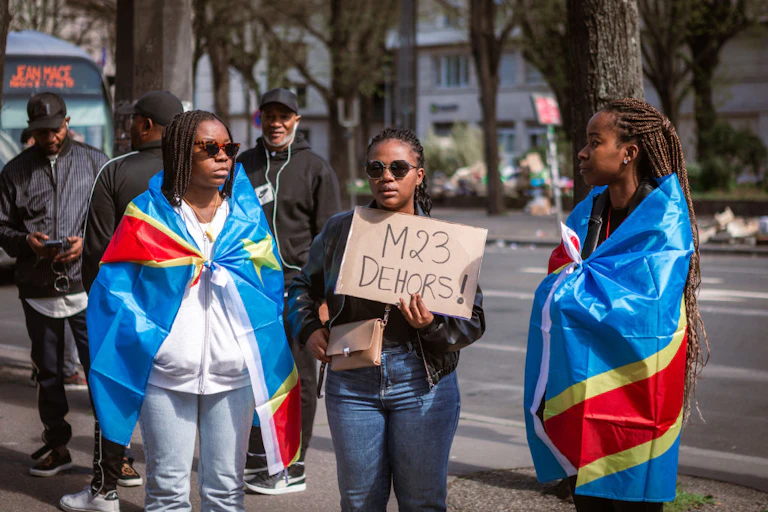 Demonstrators draped in flags hold up a placard -- which reads "M23 OUT" in French