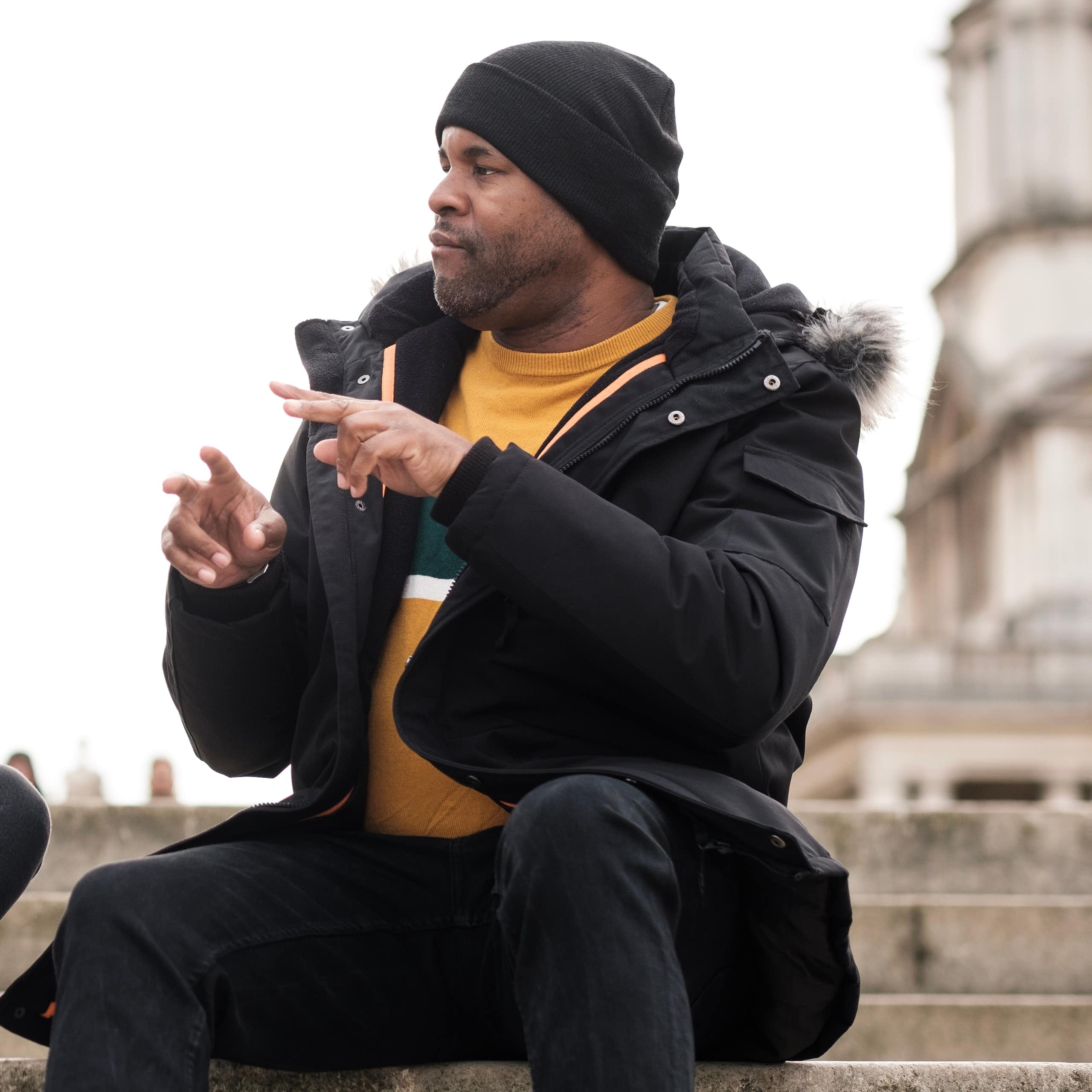 Two friends dressed in winter jackets and hats are sitting on a flight of stairs, talking in sign language