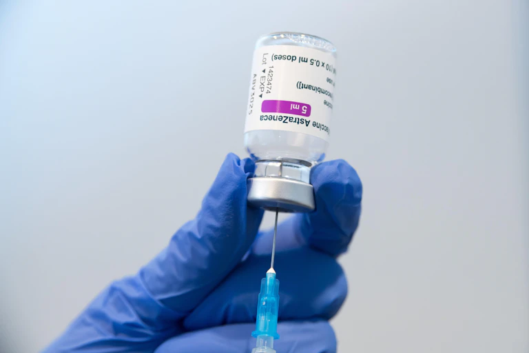 A gloved hand holding a phial of AstraZeneca vaccine