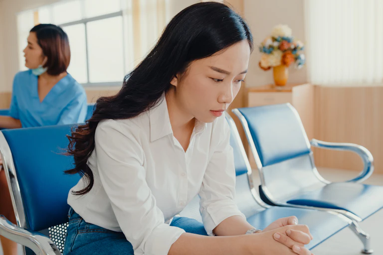 A worried looking woman sits in a hospital or GP waiting room.