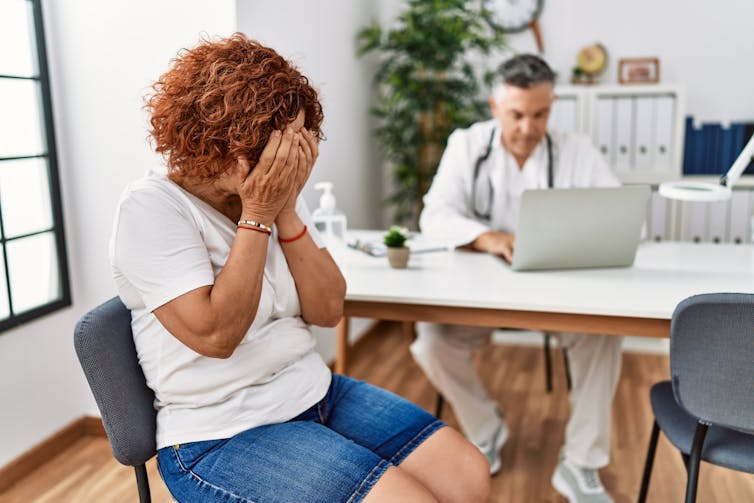 A woman covers her face with her hands while sitting in her doctor's office.