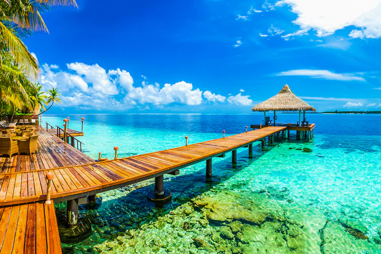 Wooden deck and pontoon of resort next to azure waters of tropical reef, blue sky