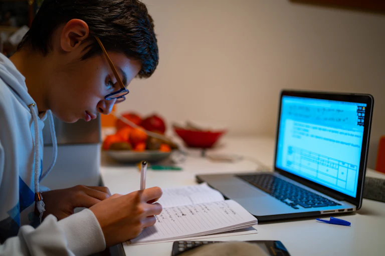 Teen boy studying taking notes from laptop